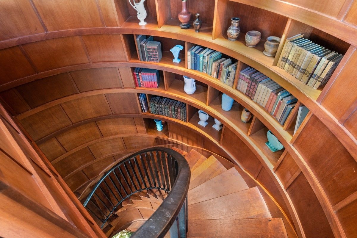 Spiral wooden staircase with built-in bookshelves, filled with books and decorative items.