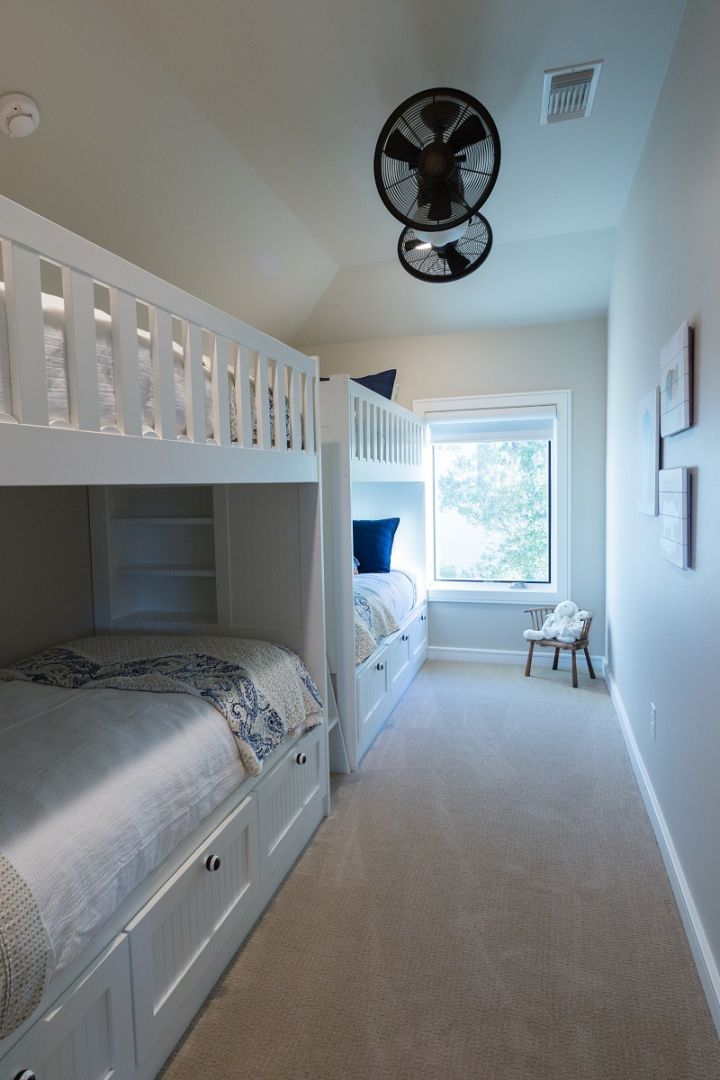 White bunk beds in a narrow room with a window and small chair, two ceiling fans.