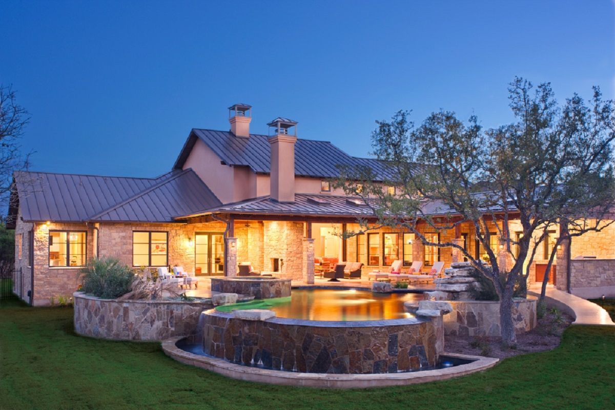 Luxury home exterior at dusk, with pool and stone facade, illuminated windows, and a manicured lawn.