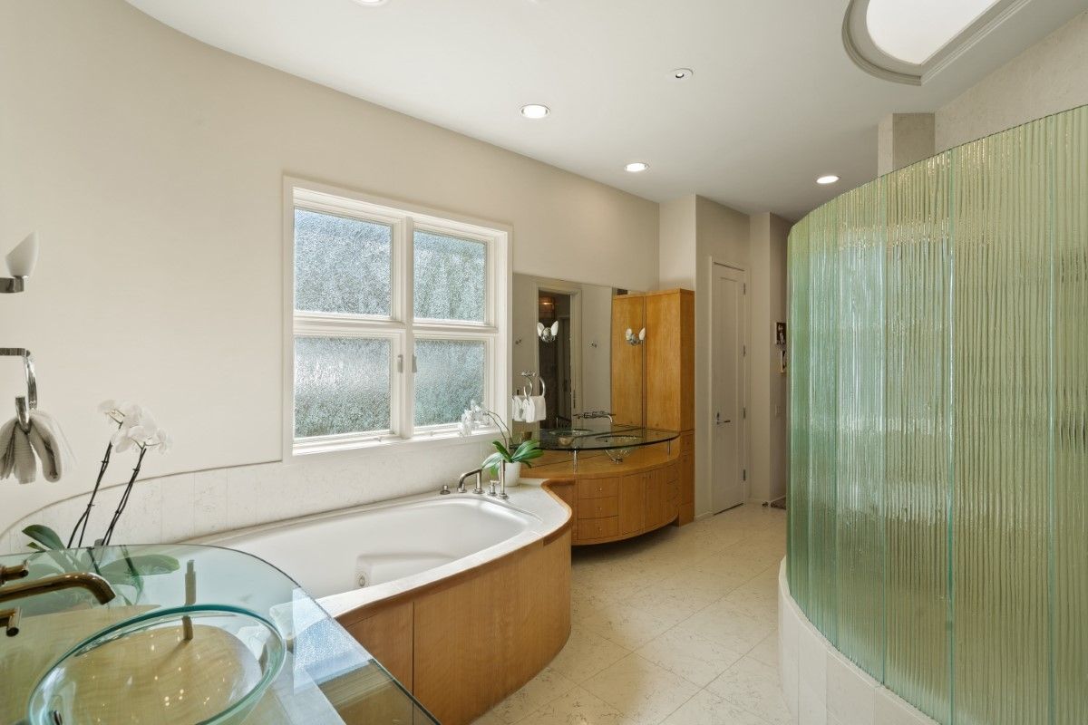 Spacious bathroom with a curved glass shower, wooden accents, a bathtub, and a window.