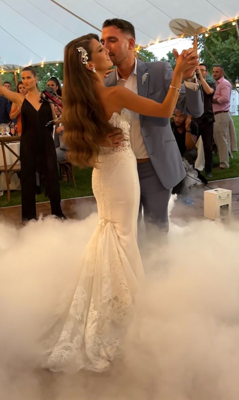 A couple in wedding attire dances on a cloud-like fog floor in an outdoor tented setting.