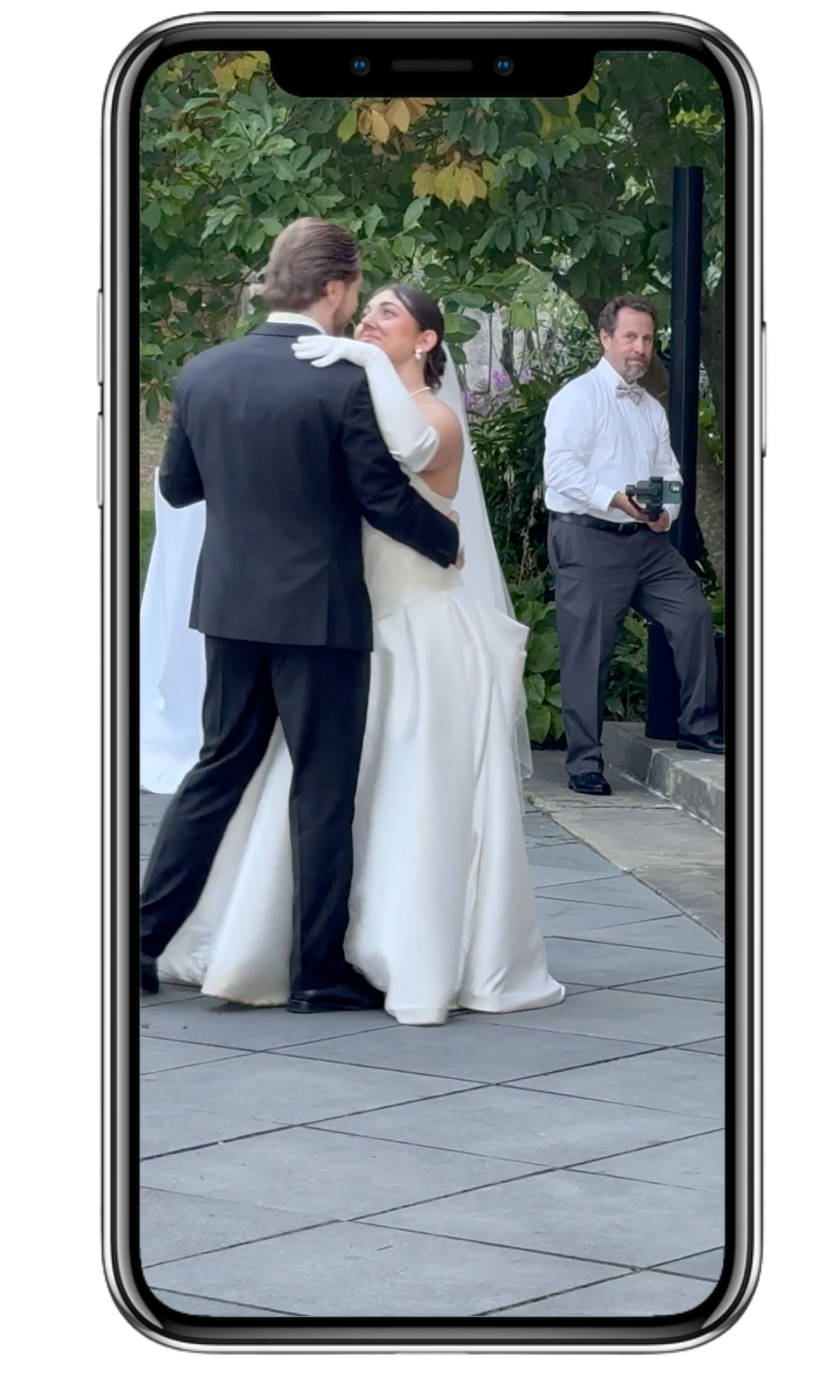 A wedding couple dances outdoors on a stone patio while a content creator captures the moment nearby.