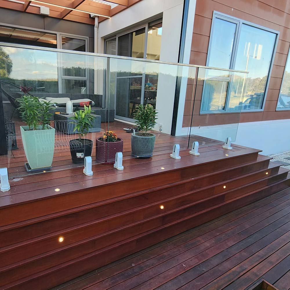 A Wooden Deck With Potted Plants and a Glass Railing — Professional Electrical & Data Pty Ltd in Bonner, ACT