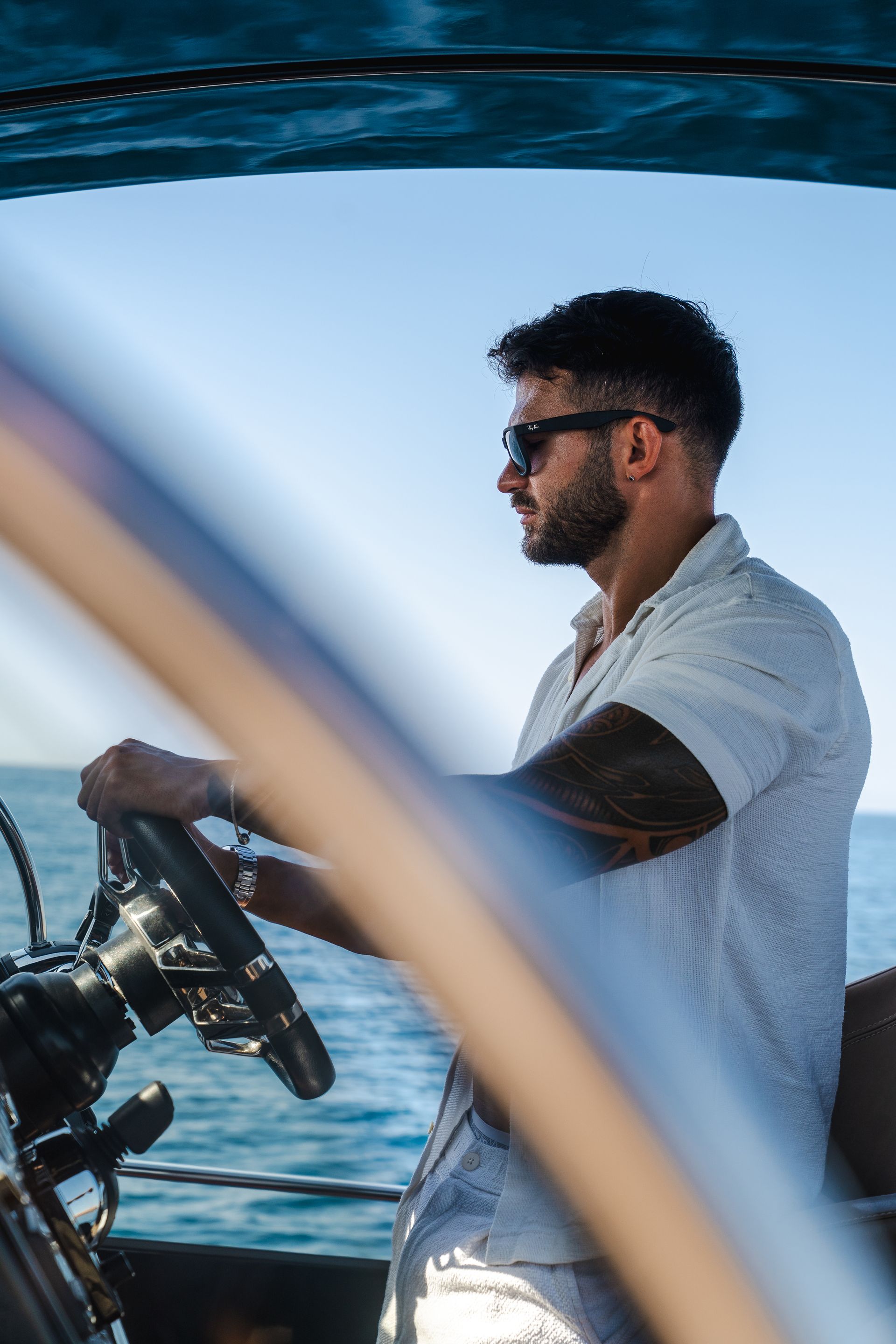 Hombre con gafas de sol dirige un barco, día soleado.