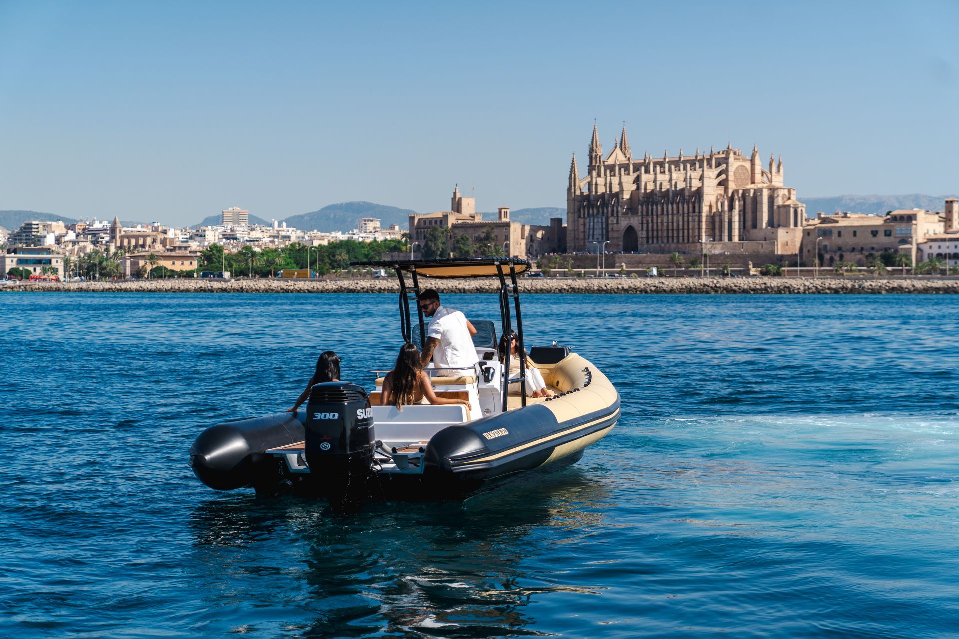 Un barco en agua azul con gente, frente a una ciudad y una gran catedral de piedra.