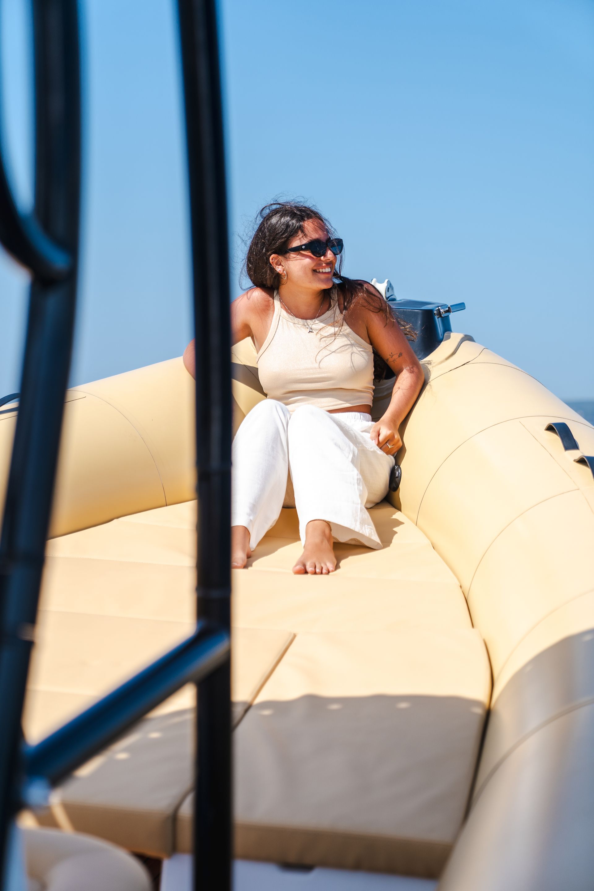 Mujer con gafas de sol en un barco, sonriendo a algo fuera de pantalla. Día brillante y soleado.