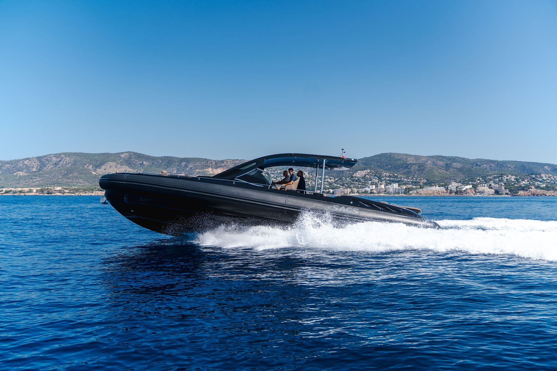 Una lancha motora negra navegando a toda velocidad por el agua azul en un día soleado cerca de una costa.