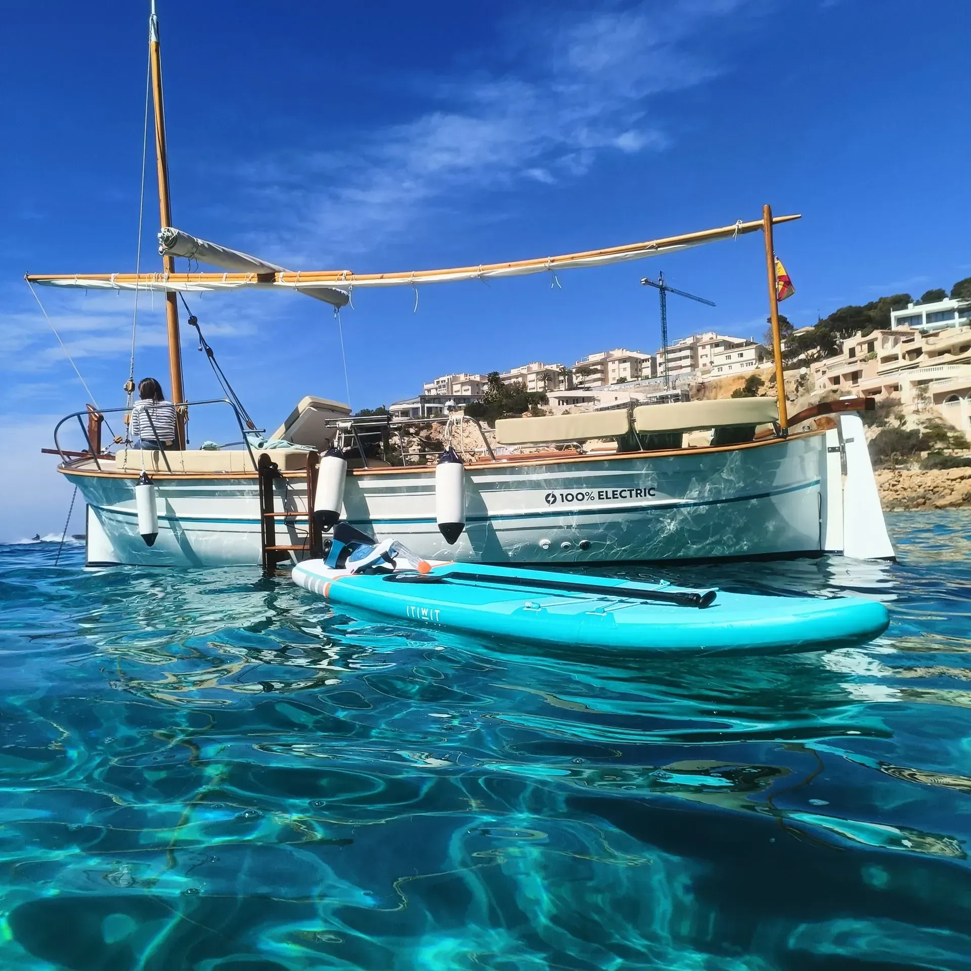 Velero y paddleboard en aguas turquesas claras; día soleado.