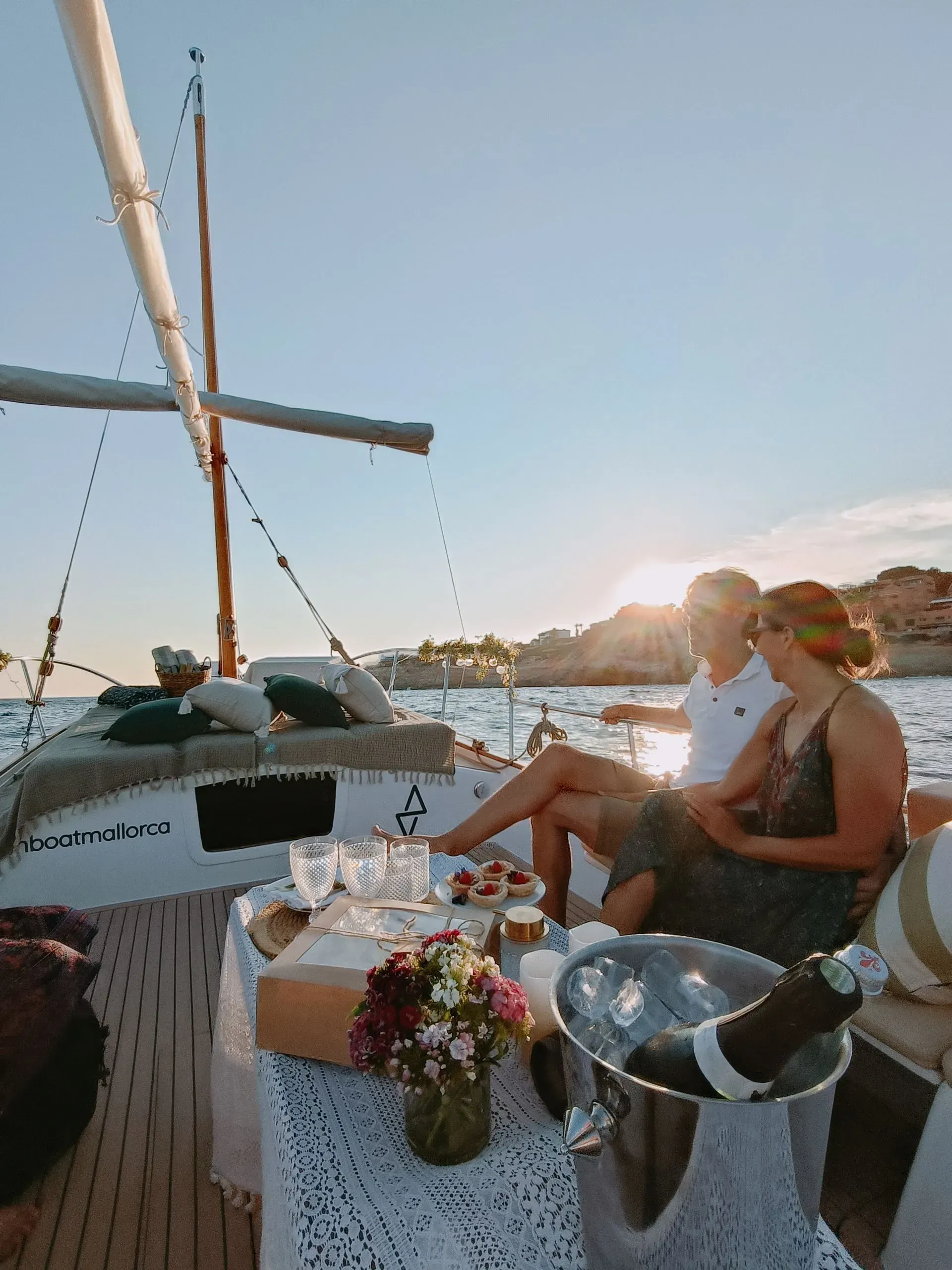 Pareja disfrutando de champán y comida en un barco al atardecer.