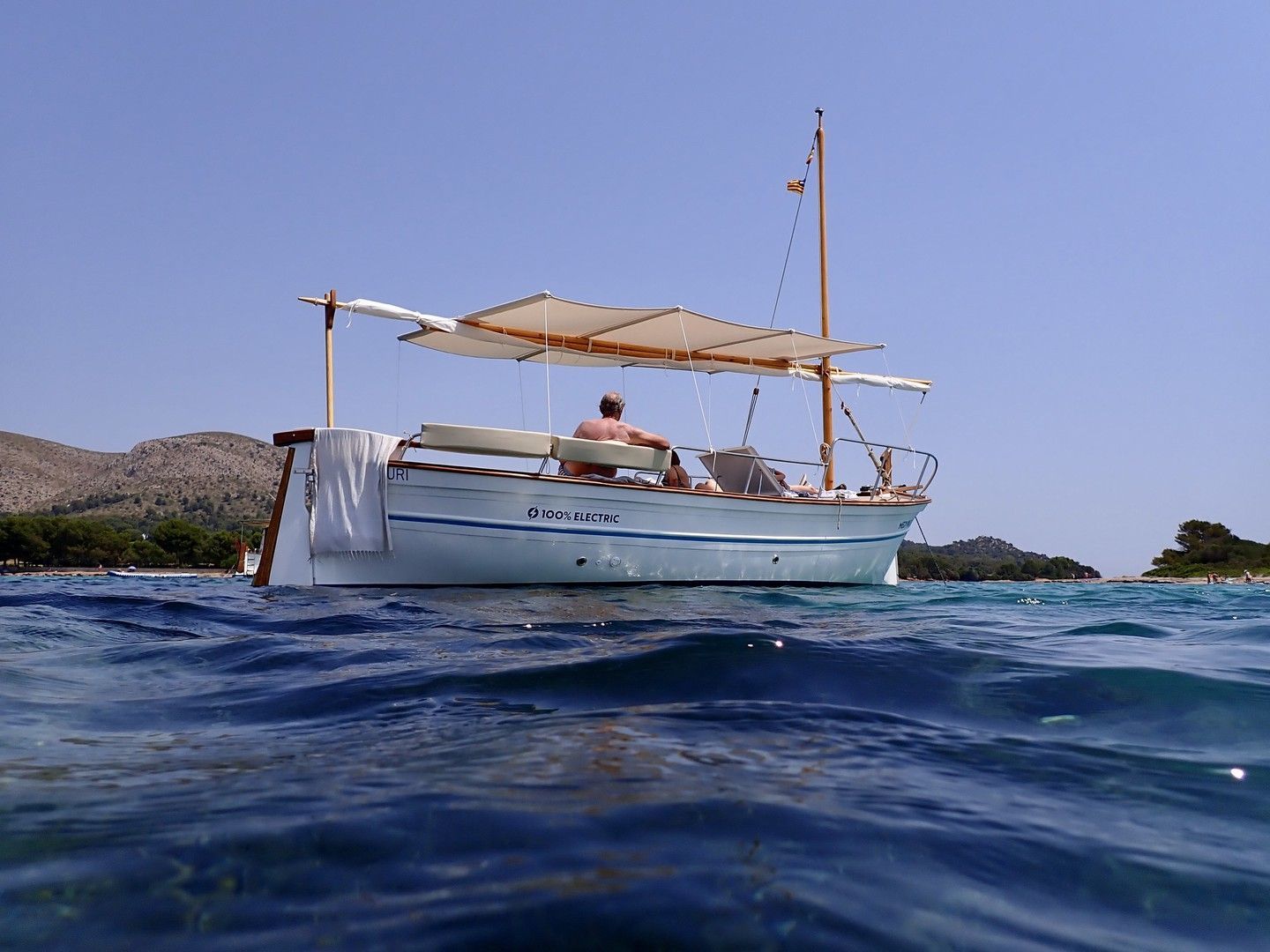 Barco en agua azul, con una persona a bordo, bajo una sombrilla de lona.