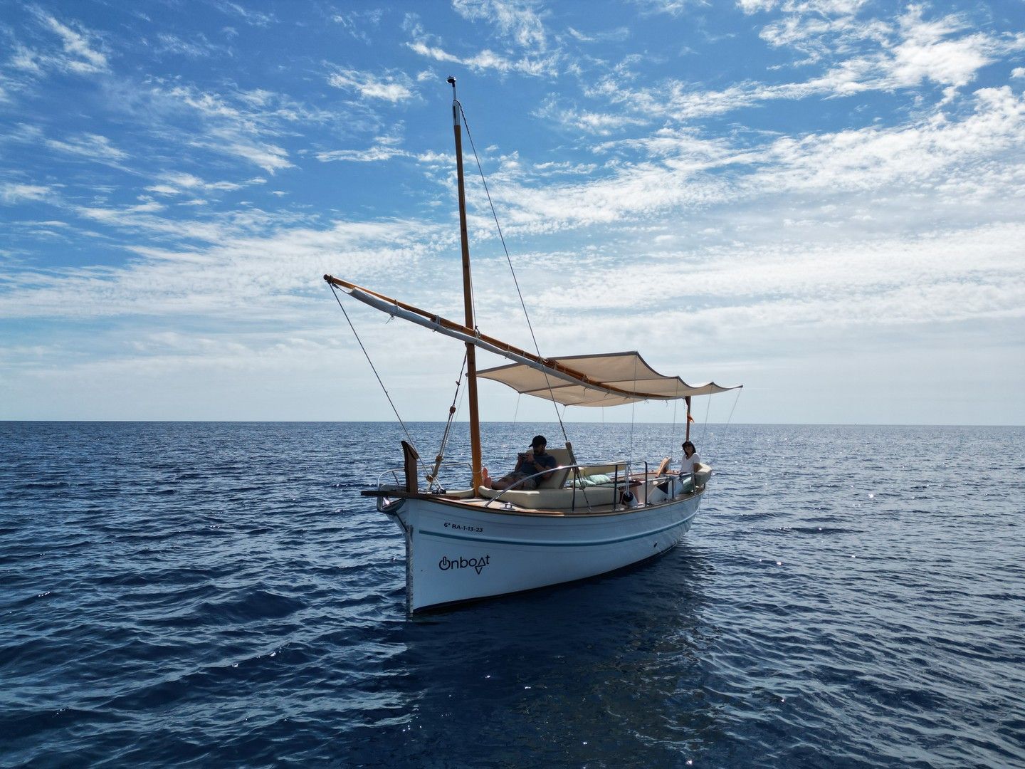 Pequeño velero blanco en agua azul bajo un cielo parcialmente nublado.