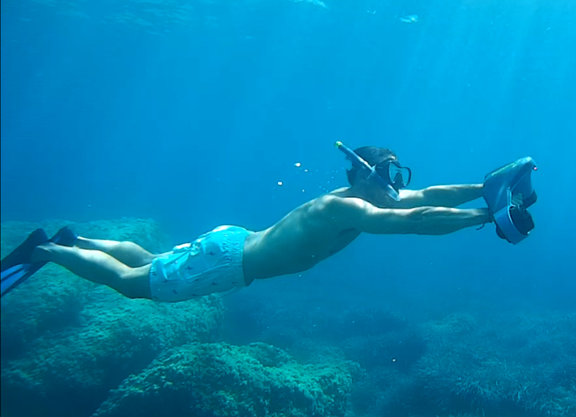 Hombre haciendo snorkel bajo el agua, con máscara, aletas y bañador, en el océano azul.
