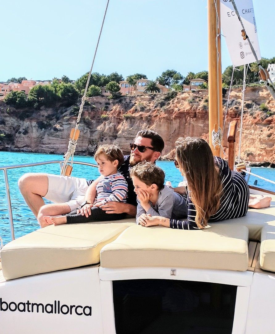 Una familia en un barco disfrutando del océano; agua azul, acantilados al fondo.