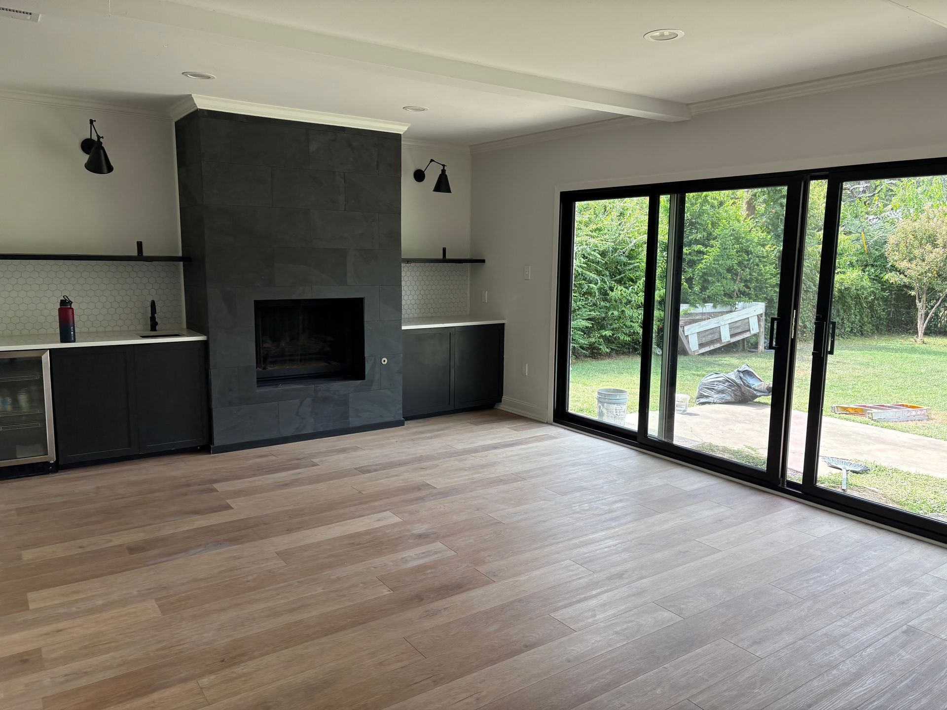Modern room with fireplace, sliding glass doors to backyard, dark cabinetry, and light wood flooring.
