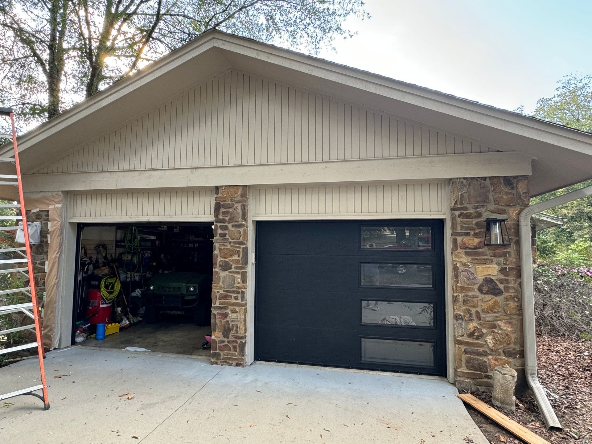 Garage exterior with open bay, dark garage door with windows, stone columns, light tan siding.