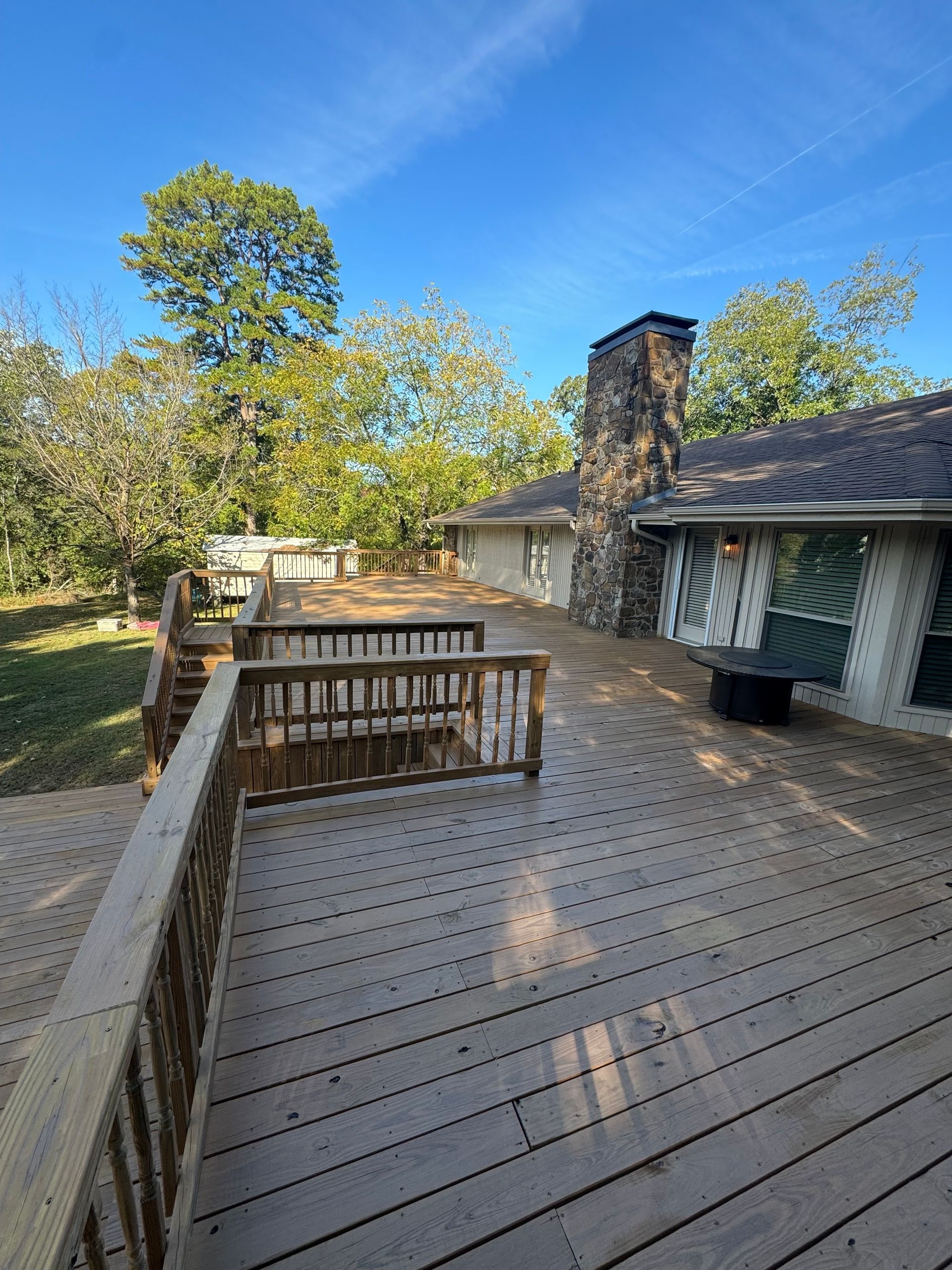 Wooden deck extends from a home with a stone chimney; blue sky and trees in the background.