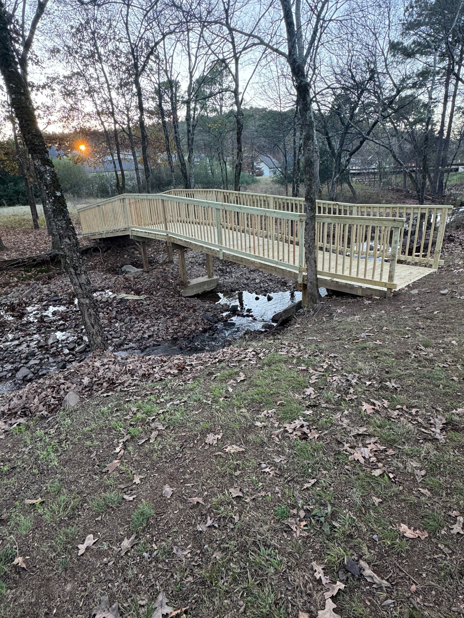 Wooden footbridge over a dry creek bed in a wooded area.