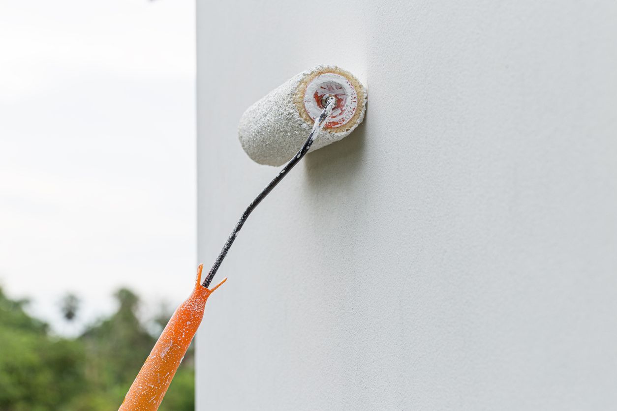 A paint roller with white paint, painting a white wall near a corner.