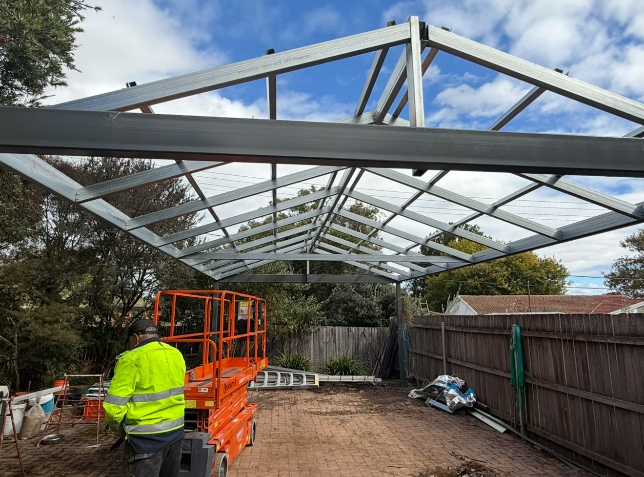 A man is standing under a metal structure in a backyard — CBR Maintenance In Tuggeranong, ATC