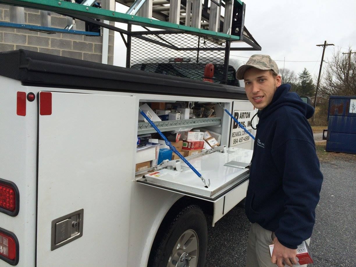 A man is standing next to a white truck with a ladder on top of it.