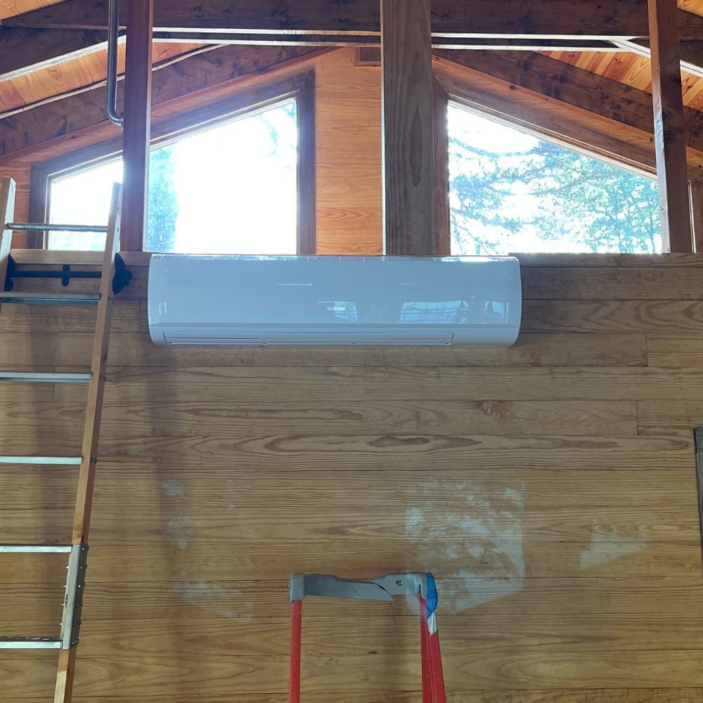 A white air conditioner is mounted on a wooden wall next to a ladder.