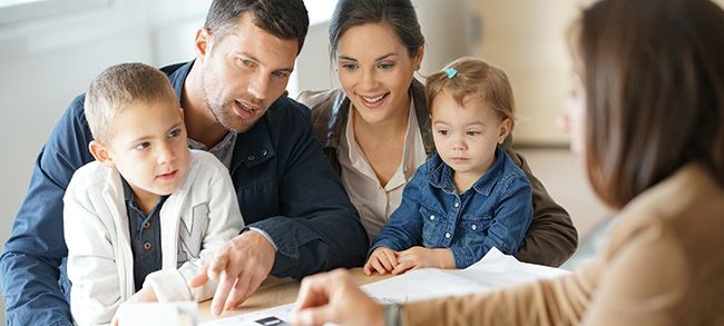 A family of four and a person at a table, looking at documents.