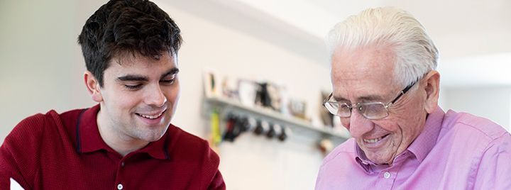 A young man is teaching an older man how to use a computer.