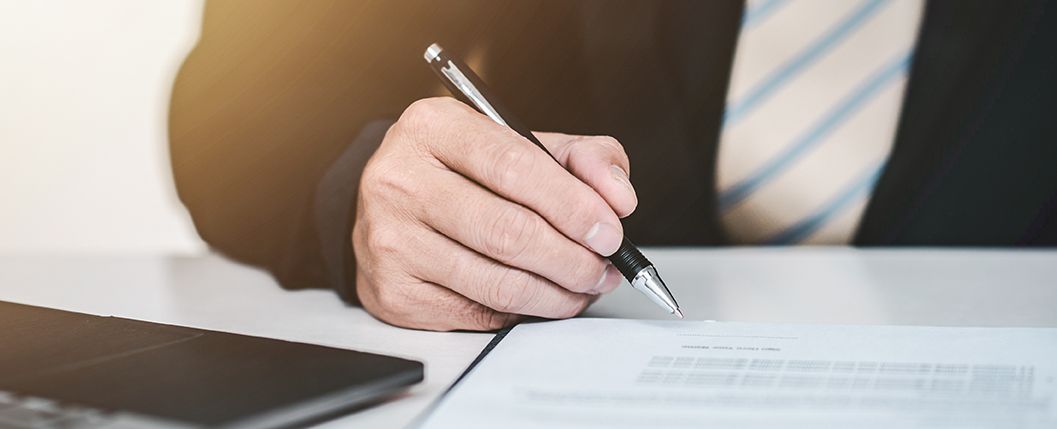 A man in a suit and tie is writing on a piece of paper with a pen.