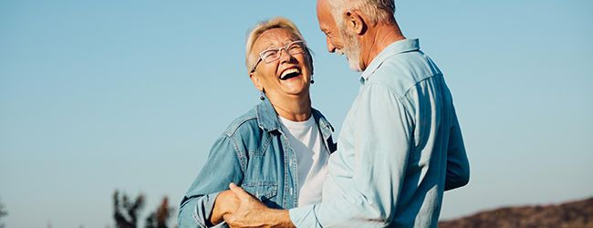 Smiling couple holding hands outdoors against a blue sky.