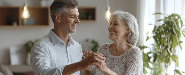 A man and an elderly woman are dancing together in a living room.