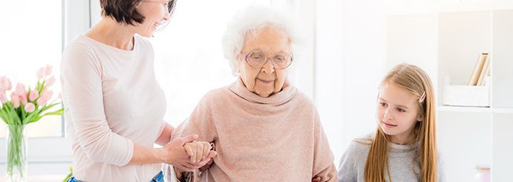 A woman is helping an elderly woman walk with a cane.