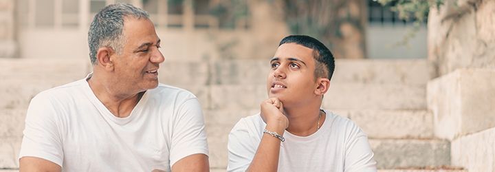 A man and a boy are sitting on a set of stairs talking to each other.