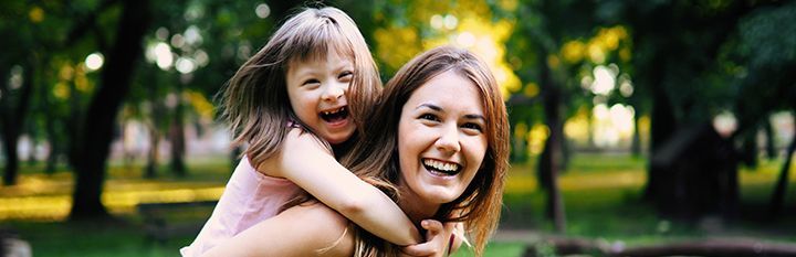 A woman is carrying a little girl on her back in a park.