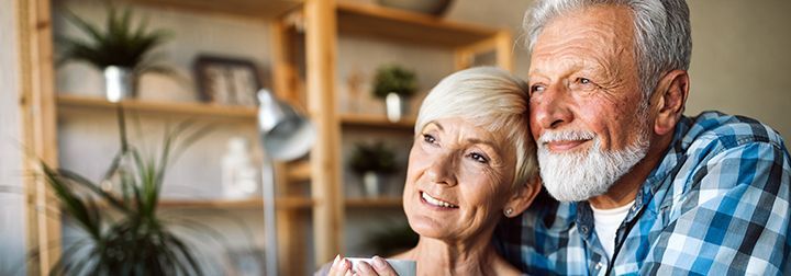 An elderly couple is sitting next to each other in a living room.