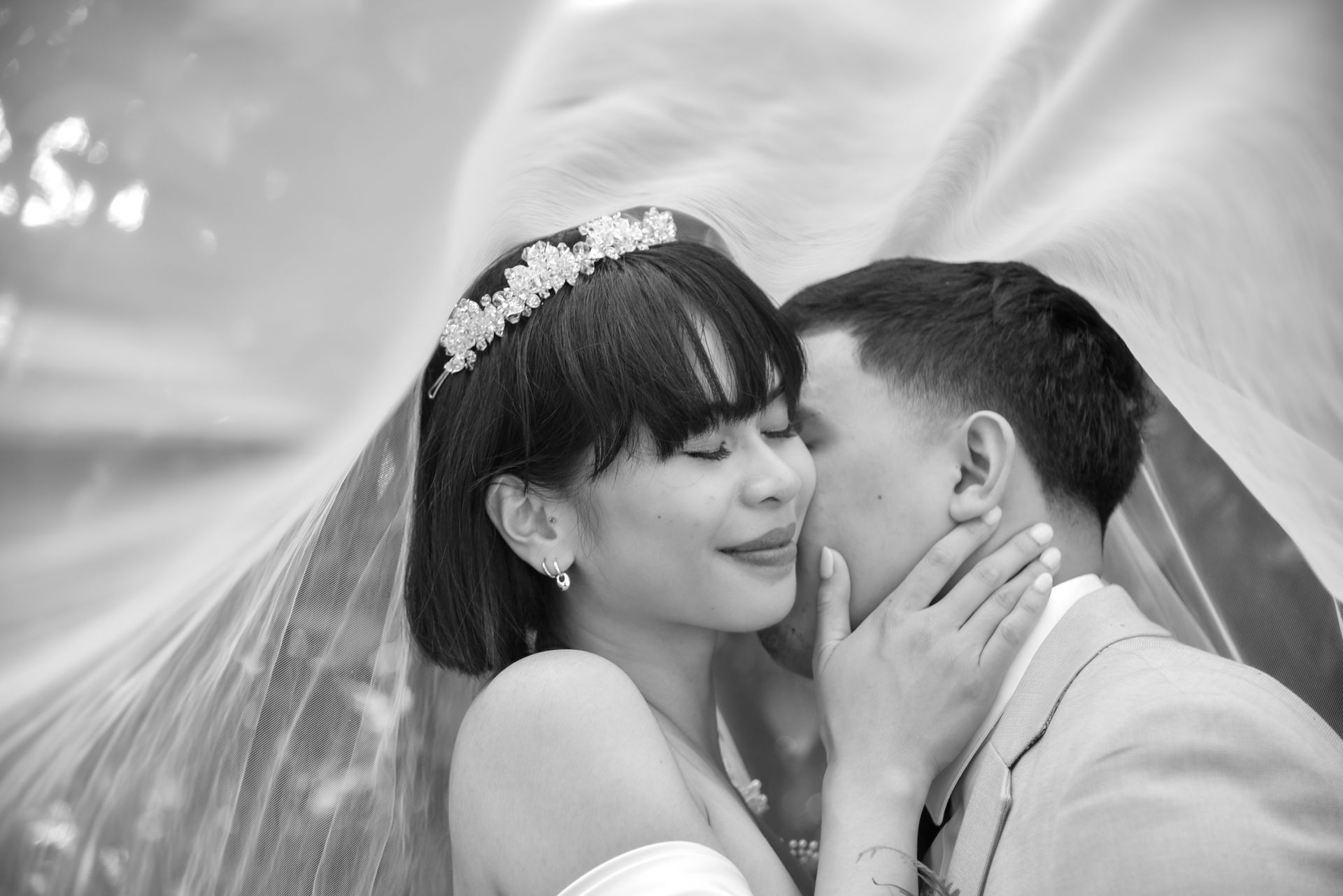 Bride and groom laugh, holding hands, in a church. She wears a white gown and veil; he wears a black suit.