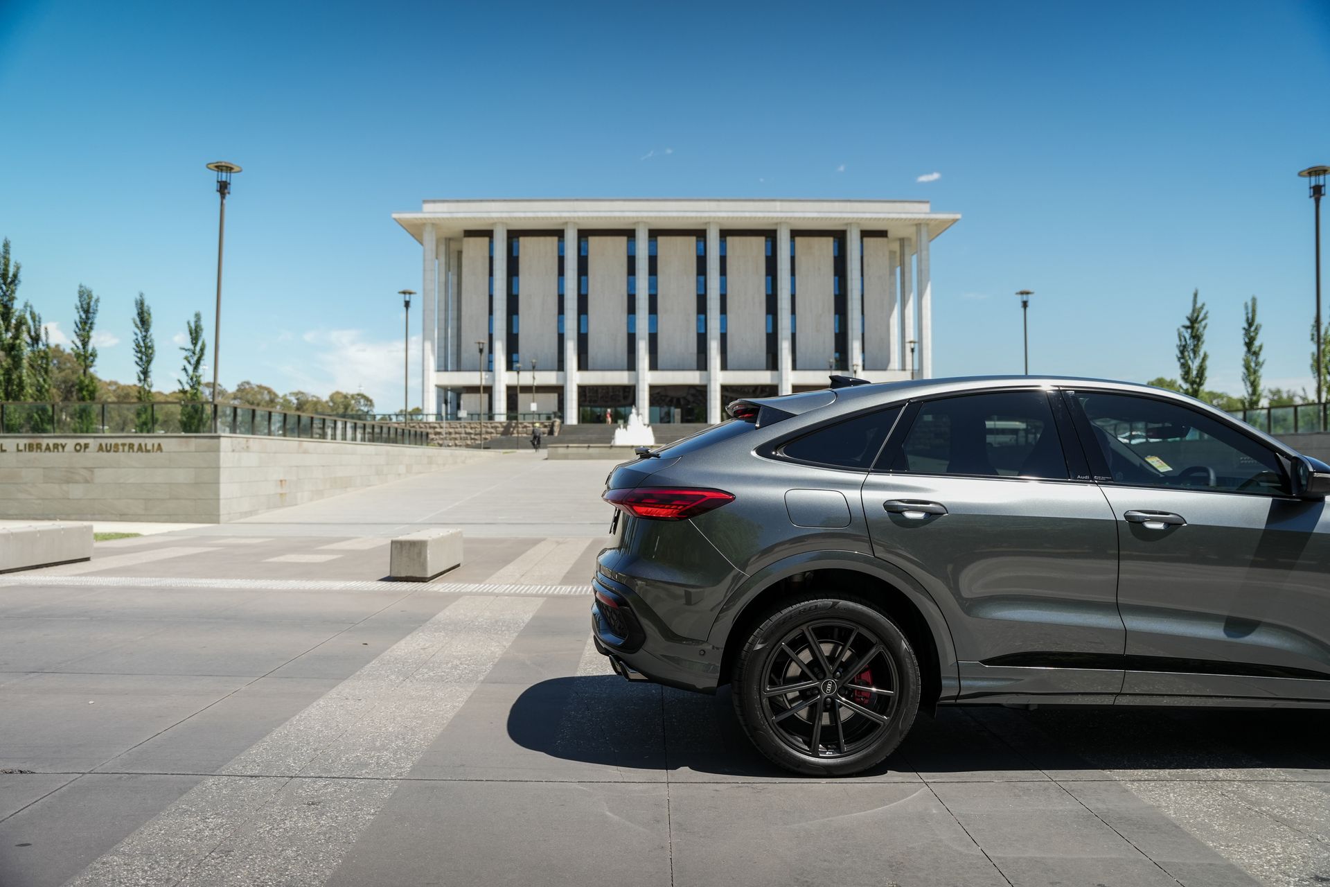 White sports car parked on asphalt, near trees and buildings, with the sun shining.