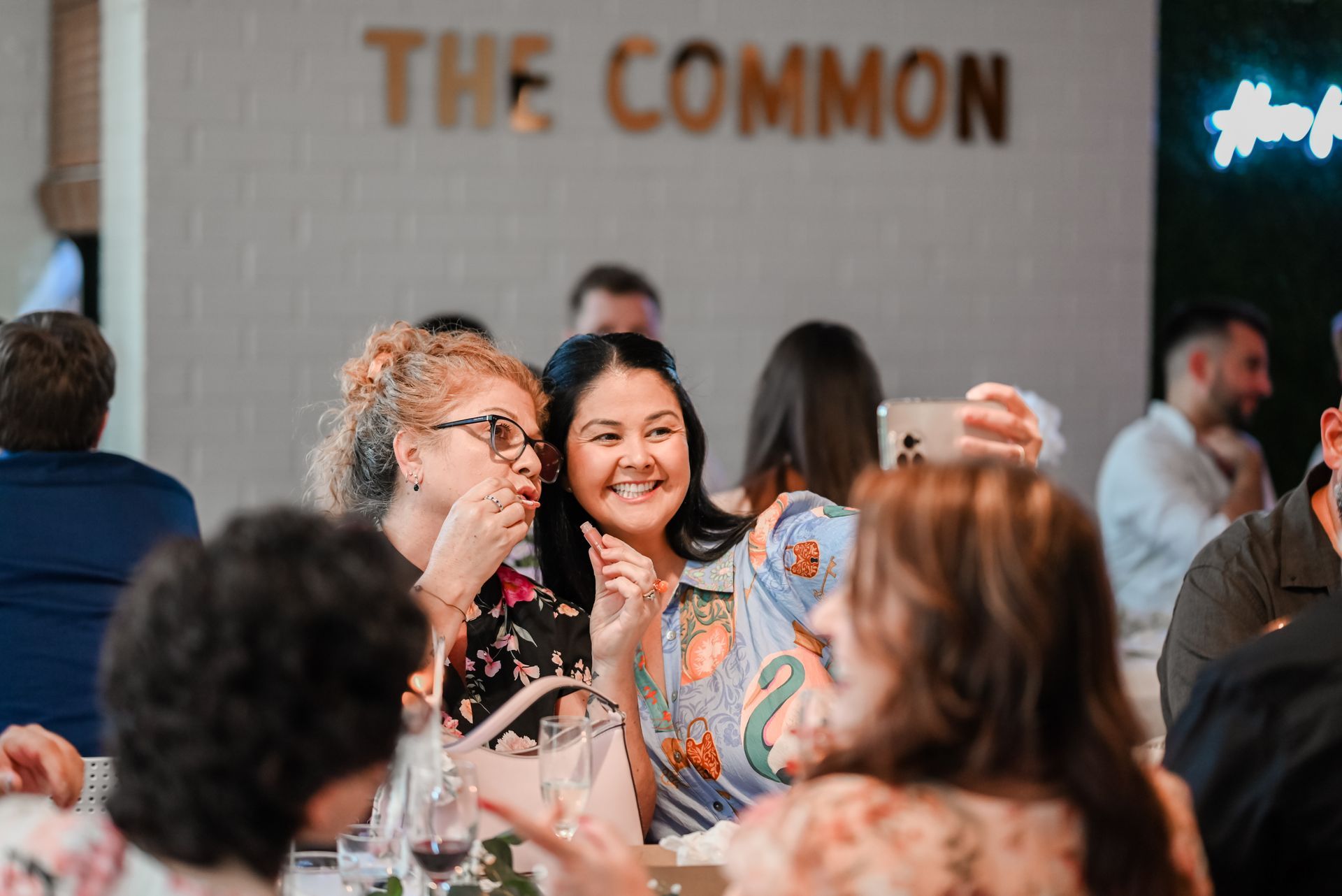 Woman smiling with long blonde hair, small gold earring, in a colorful setting with lights.