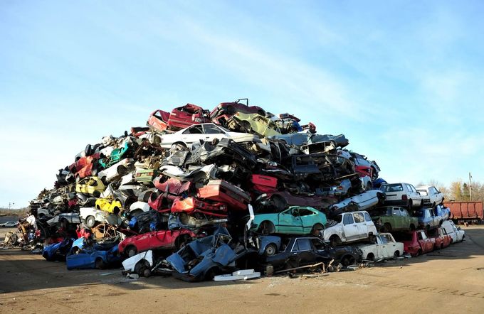 Un cumulo di auto accartocciate ammassate in una discarica sotto un cielo azzurro e limpido.