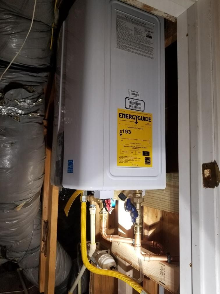 White tankless water heater installed on a wall. Yellow gas line and copper plumbing visible.
