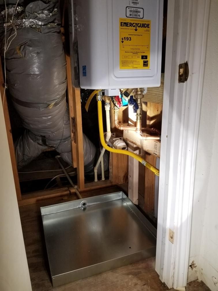 A small utility closet with a tankless water heater, gas lines, and a drain pan.