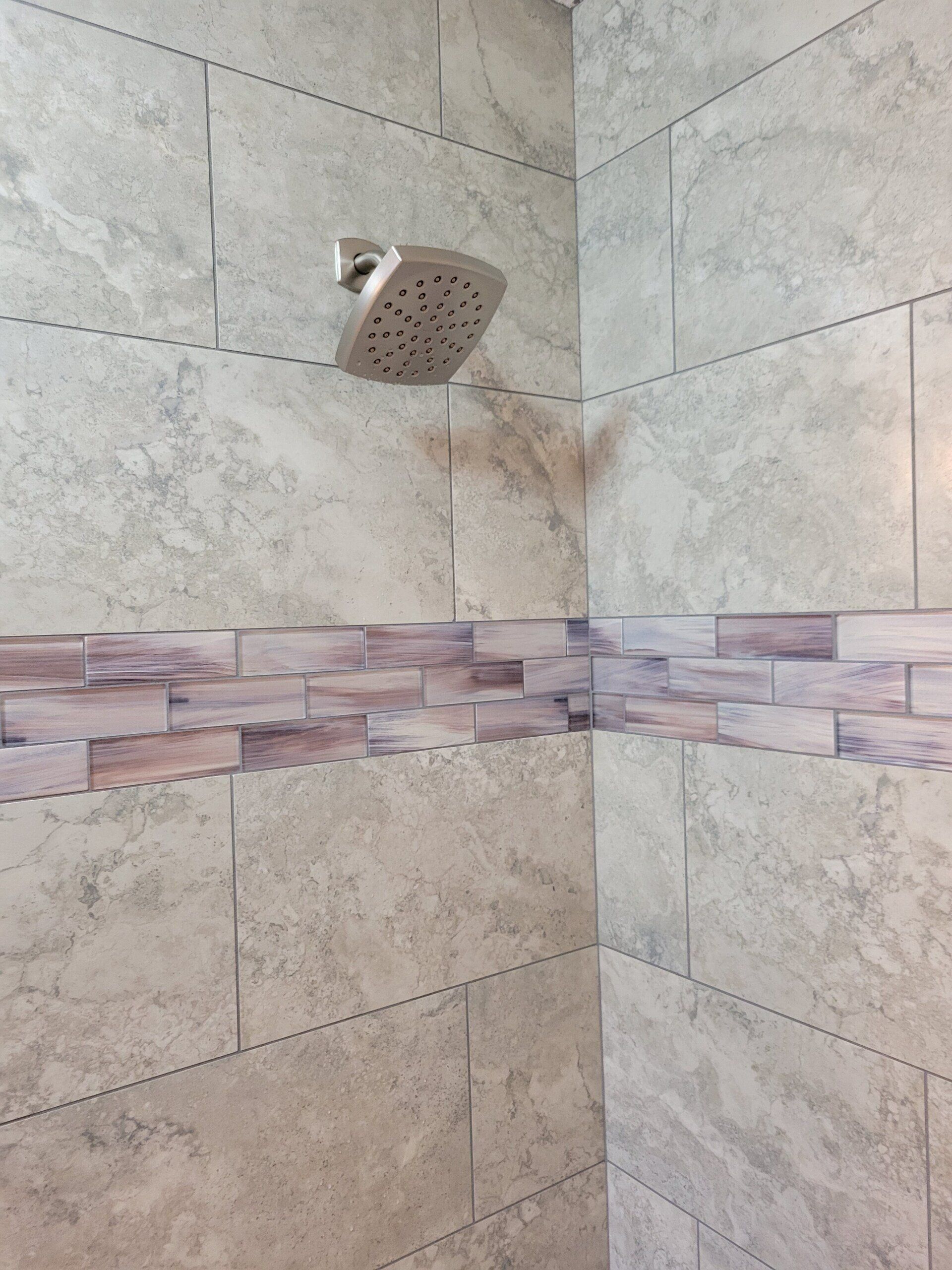 Shower with light gray tile walls, mosaic tile border, and a silver showerhead.