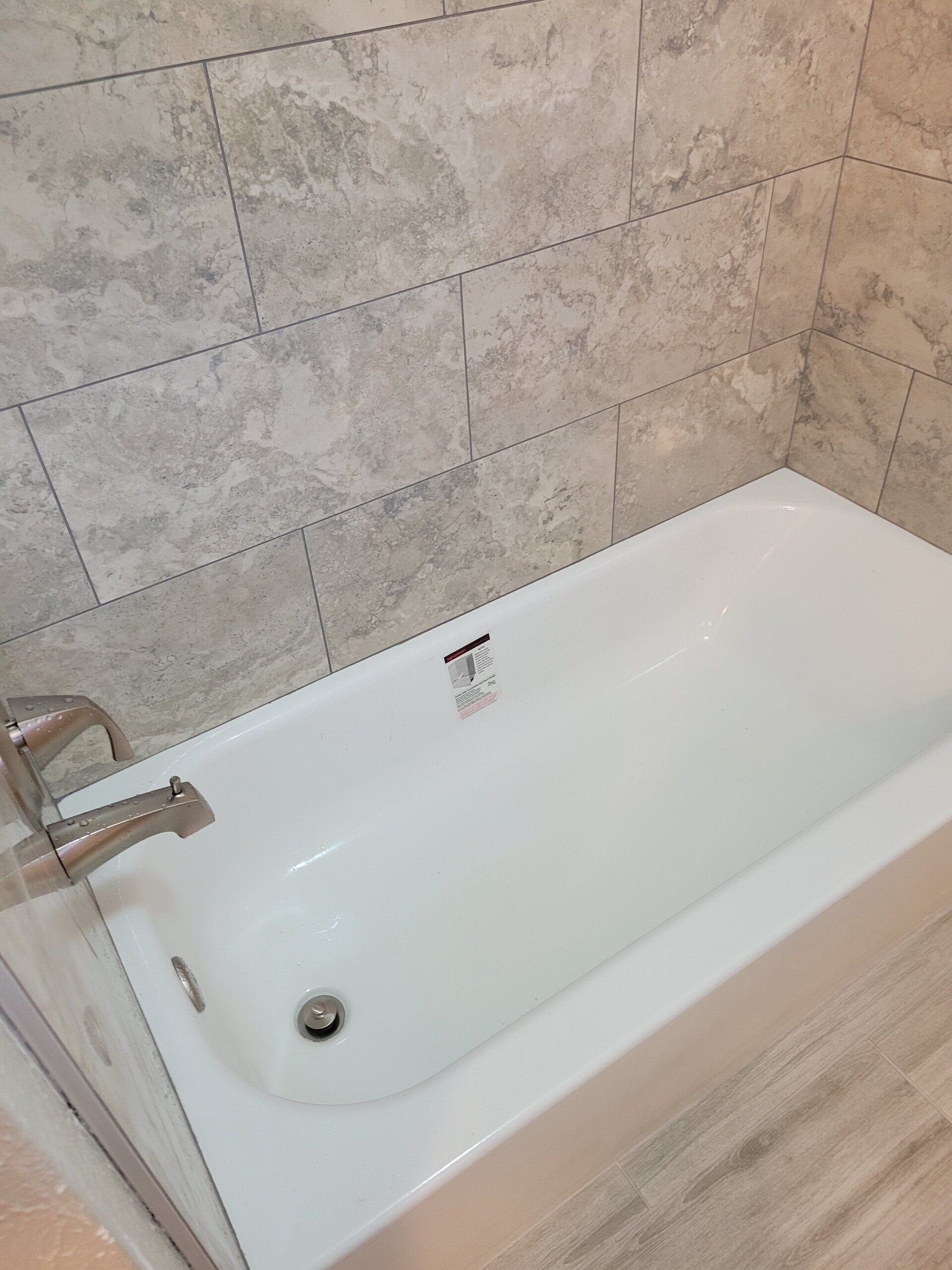 White bathtub with silver faucet, grey tiled walls and floor.