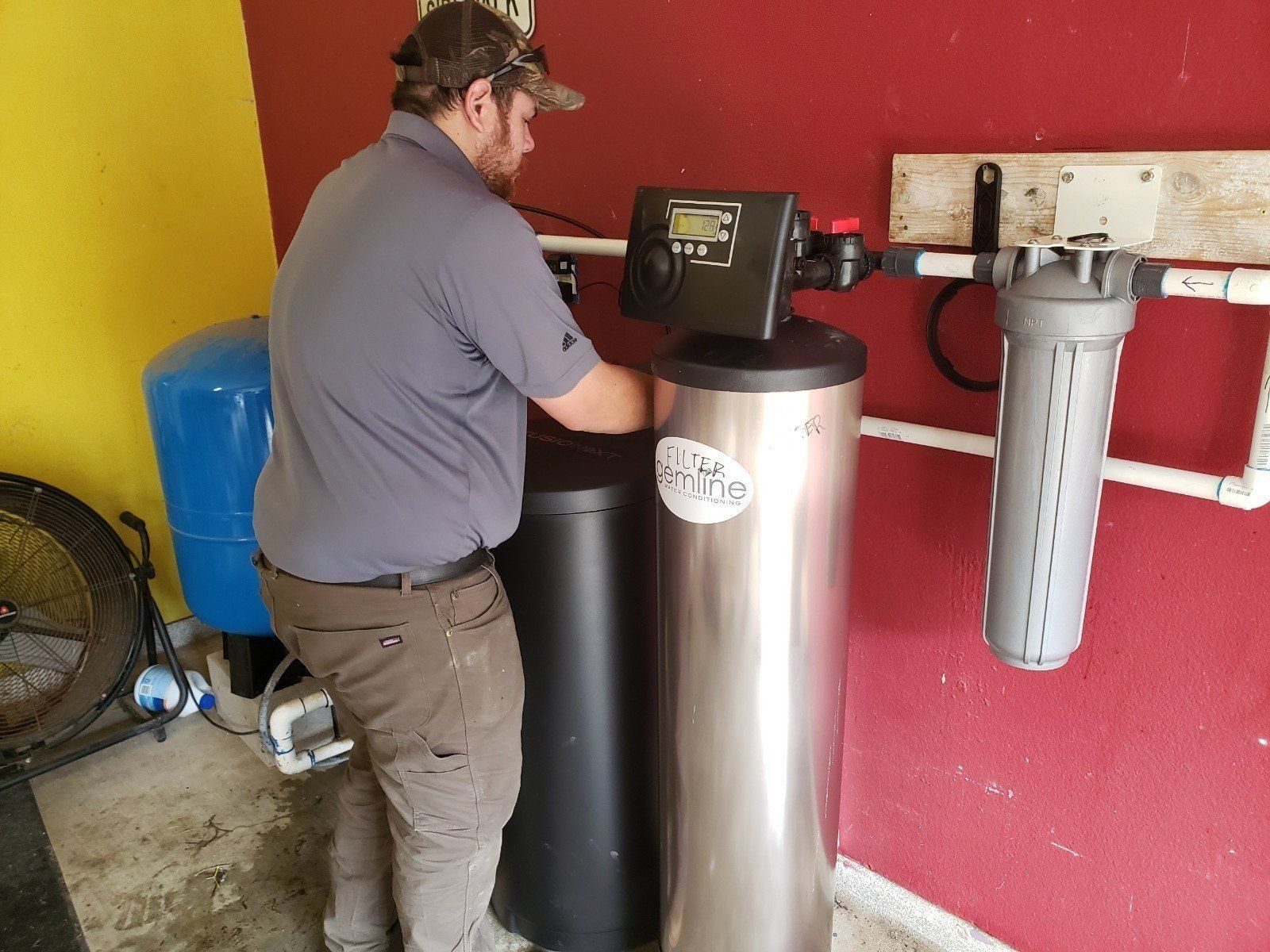 Man in a cap working on water filtration system in a garage.