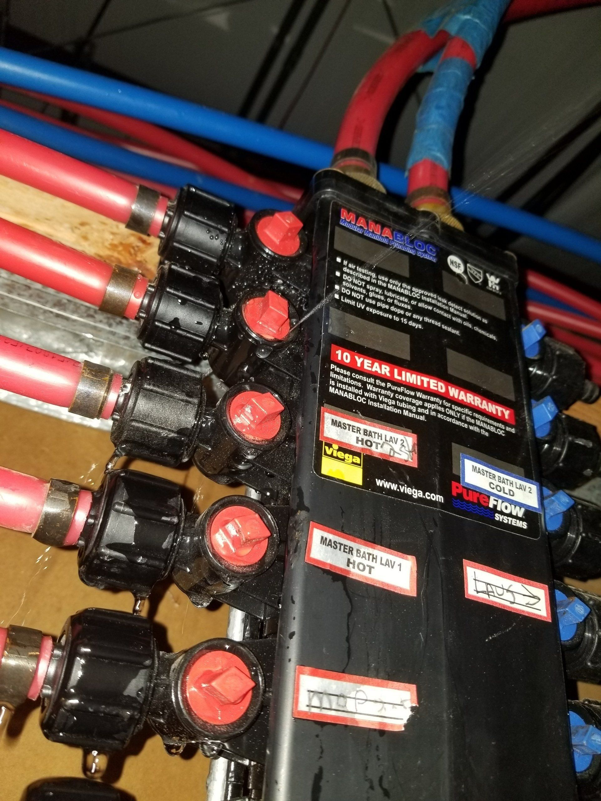 A black manifold with red and blue pipes and red valve handles, likely for water distribution.