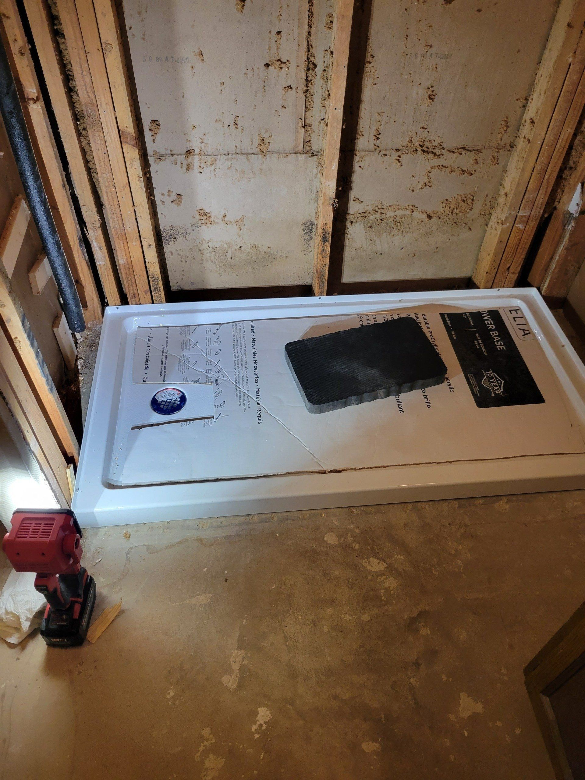 White shower base installed in unfinished basement with framing and a red drill.