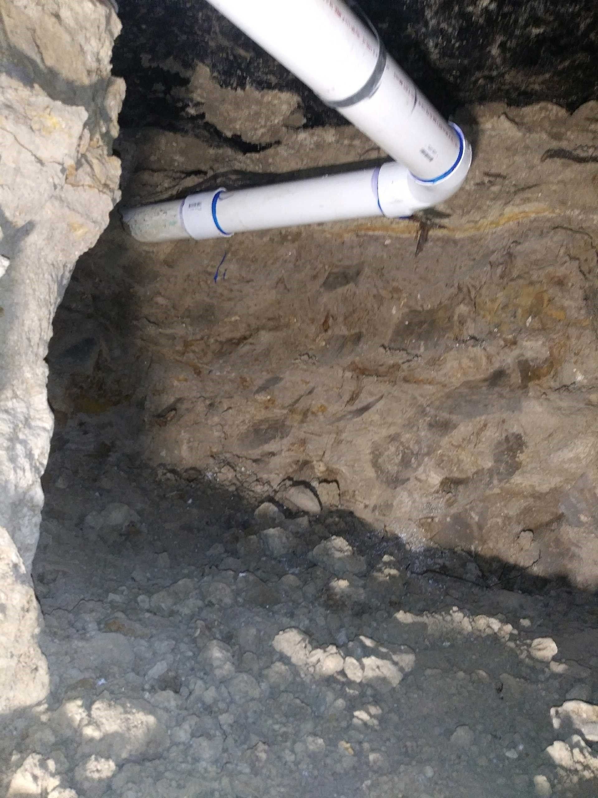 White PVC pipes in a hole in a rocky, earthen wall.