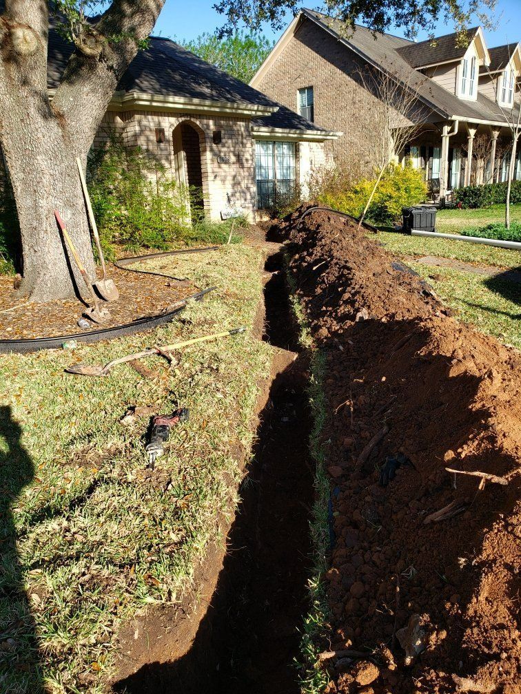 Narrow trench dug in a yard, leading toward a house. Brown dirt piled along the trench's edge.