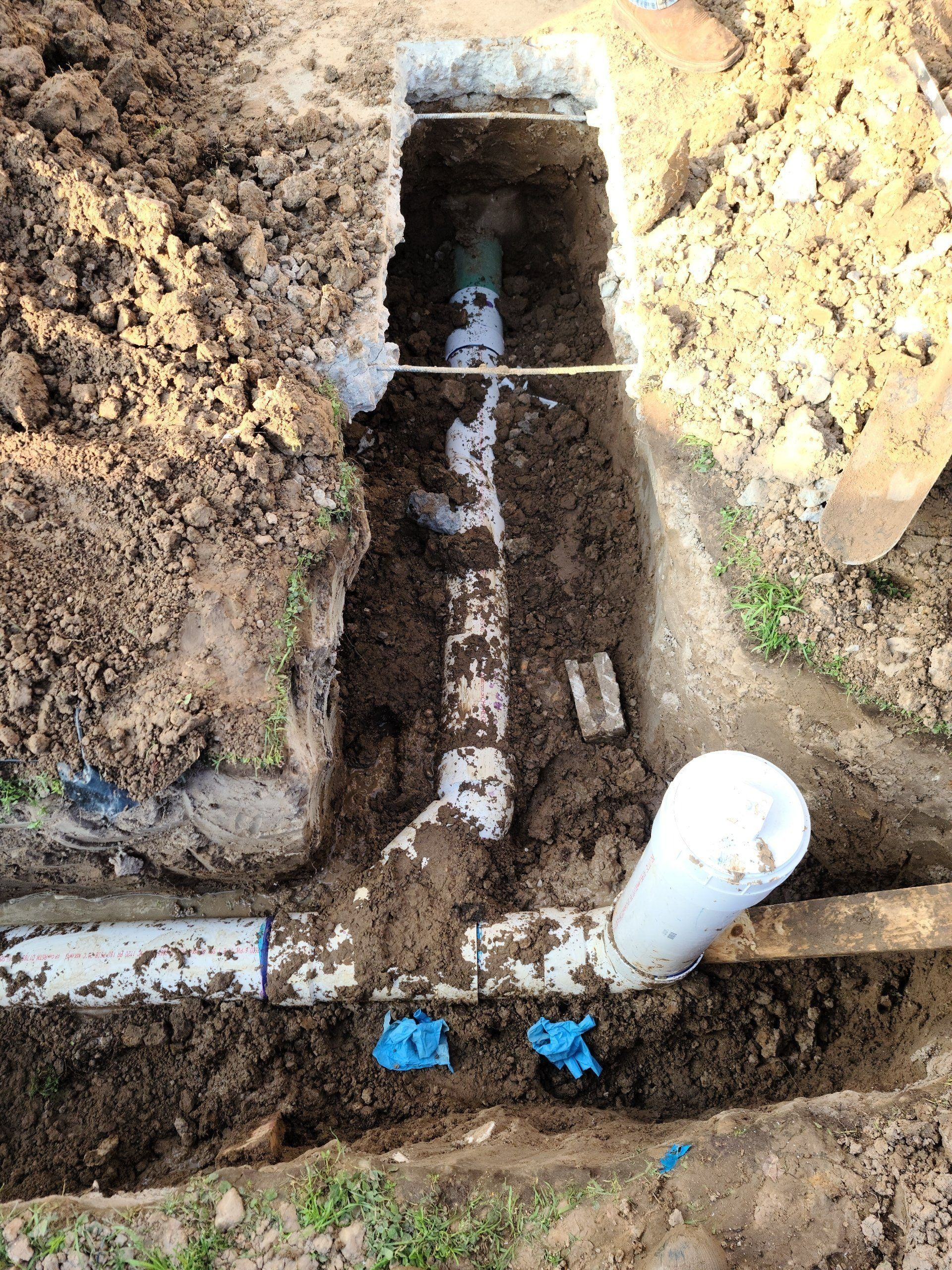 Trench with exposed white and green PVC pipes in the ground, showing plumbing repair in progress.