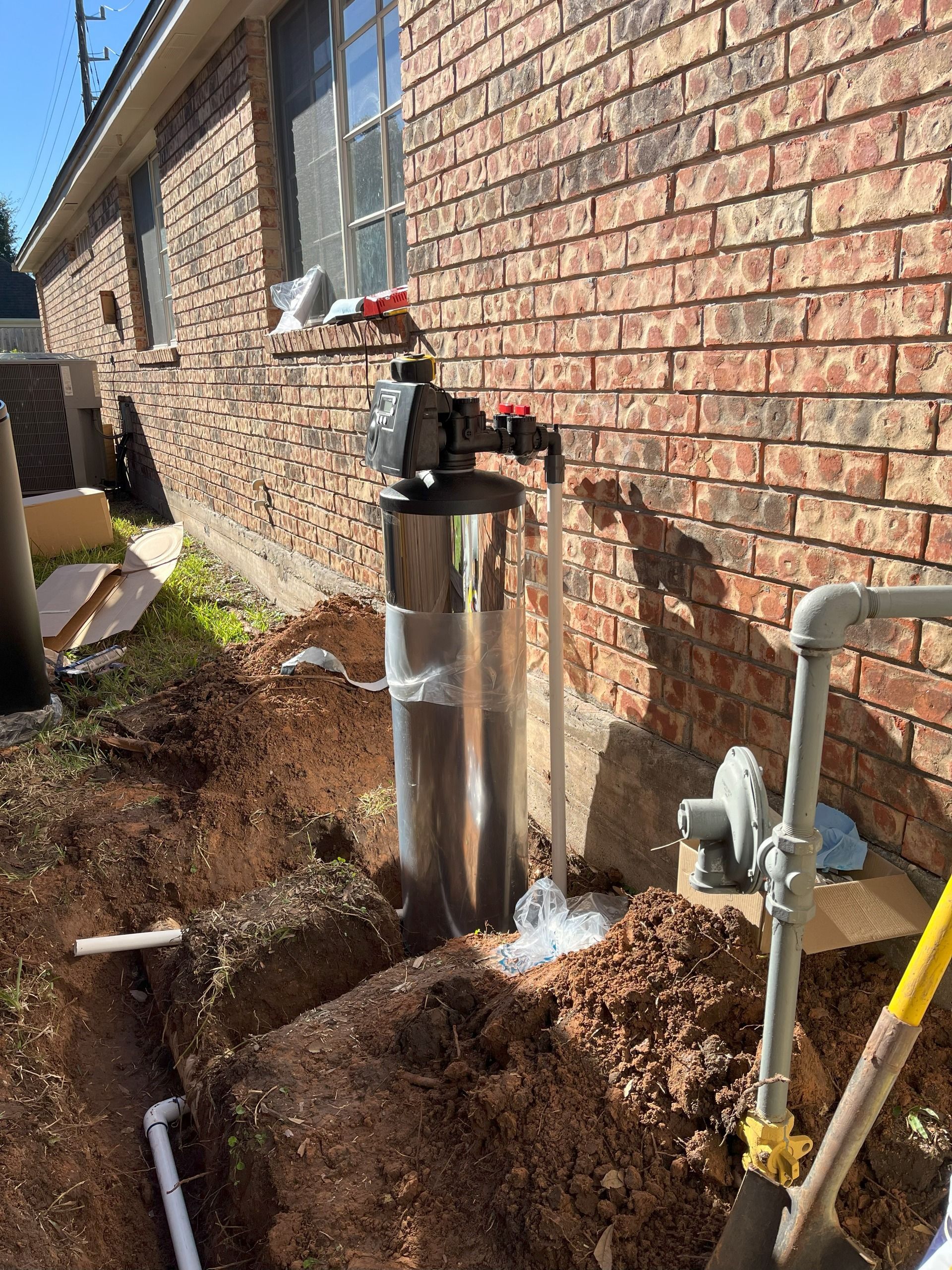 Well water system installation outdoors; stainless steel tank, exposed piping, digging around the foundation.