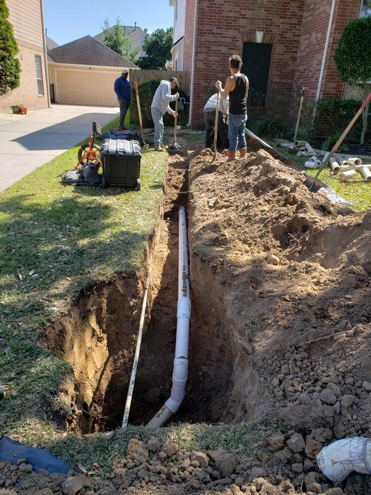 Workers installing a white pipe in a trench on a residential lawn. The house is brick.